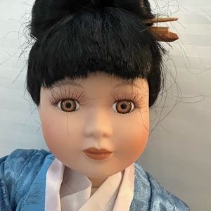 Porcelain oriental doll kneeling on a satin pillow with beautiful Asian outfit